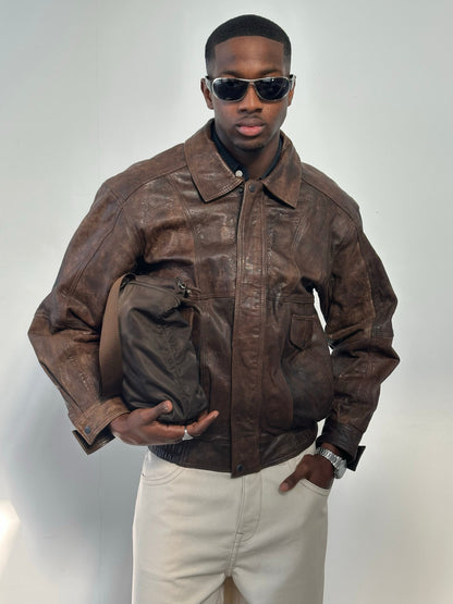 Vintage 1990s distressed leather bomber jacket, size M, with worn-in details and classic style, displayed on a hanger.
