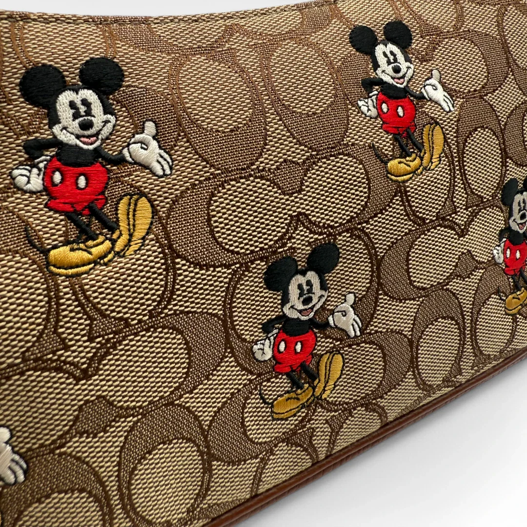 https://cdn.shopify.com/s/files/1/0564/9376/8855/files/Coach_x_Disney_Handtasche_Pochette_mit_Umhaengegurt_monogram_braun_vintage_luxury_handbag_2620.webp?v=1743622420