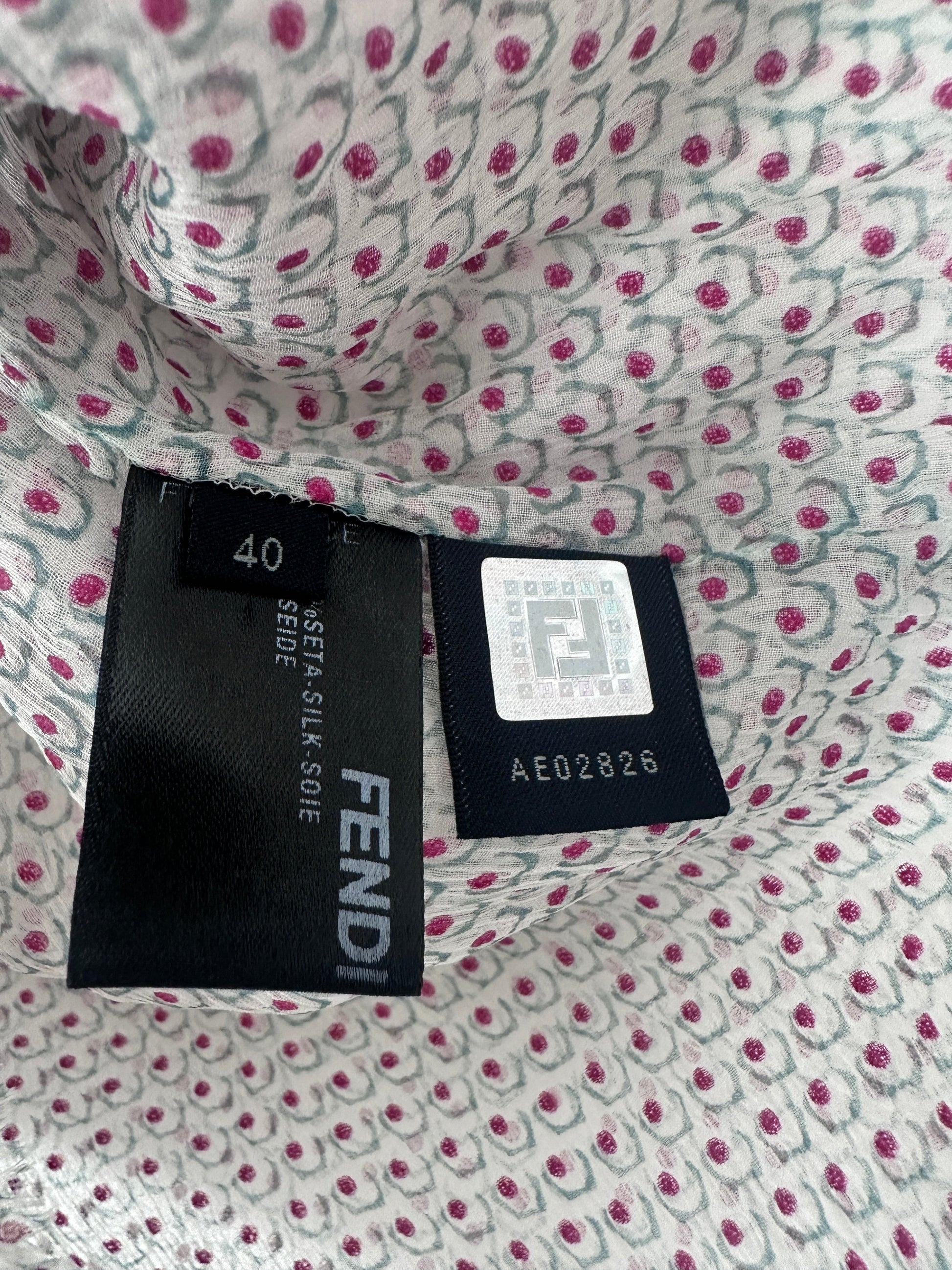 Close-up of a Fendi clothing tag sewn onto patterned fabric. The tag is black with white text reading FENDI and size 40, while the fabric has a white base with pink and gray floral motifs.