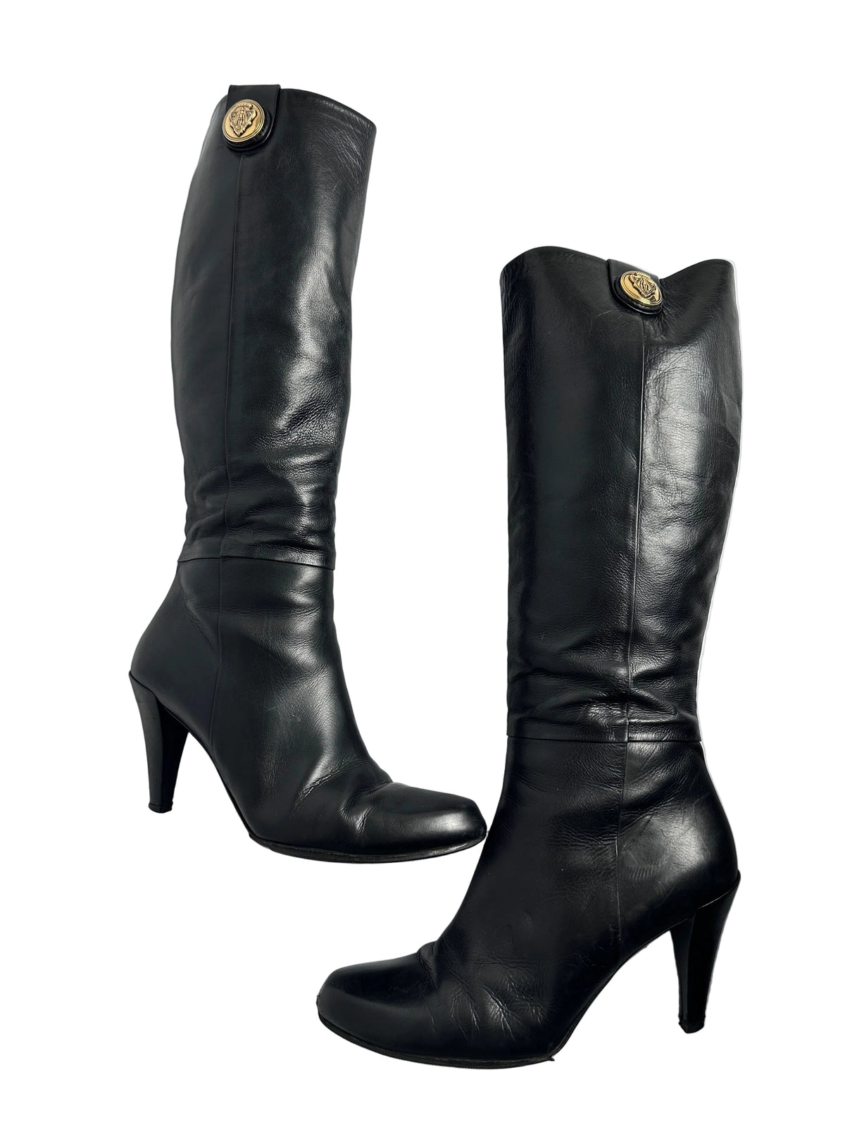 Pair of black leather knee-high boots with gold buttons on a white background