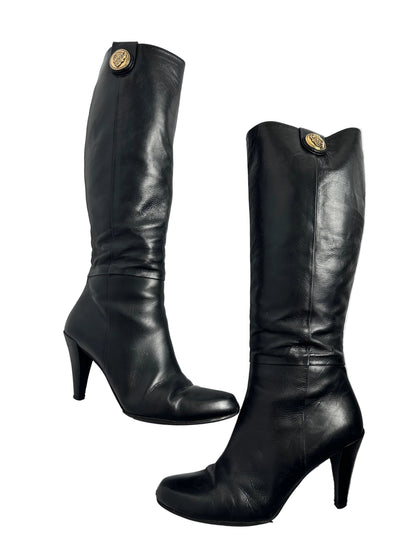 Pair of black leather knee-high boots with gold buttons on a white background