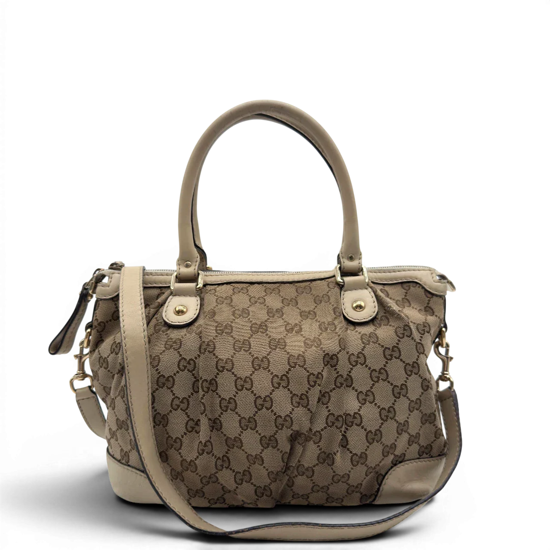 https://cdn.shopify.com/s/files/1/0564/9376/8855/files/Gucci_Handtasche_Sukey_mit_Umhangegurt_monogram_beige_vintage_GG7929.webp?v=1779966403