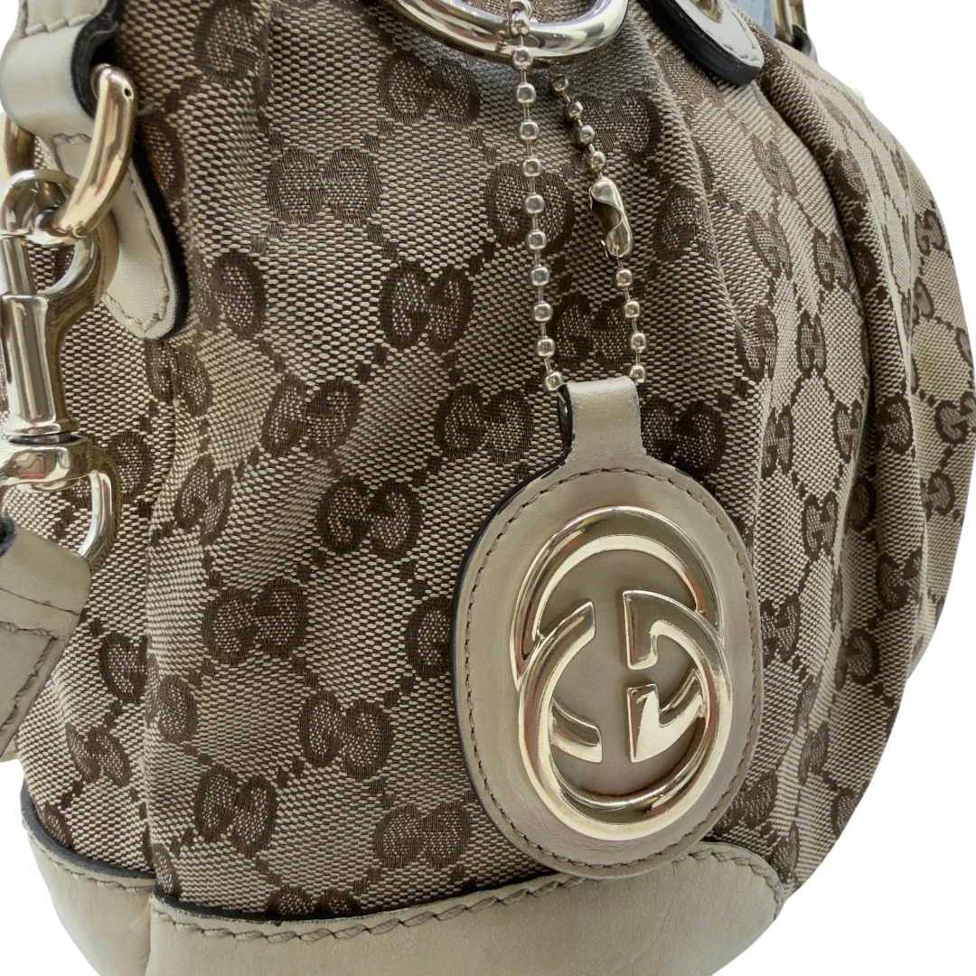 https://cdn.shopify.com/s/files/1/0564/9376/8855/files/Gucci_Handtasche_Sukey_mit_Umhangegurt_monogram_beige_vintage_GG7938.webp?v=1779966403