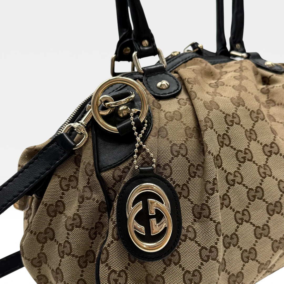 https://cdn.shopify.com/s/files/1/0564/9376/8855/files/Gucci_Handtasche_Sukey_mit_Umhangegurt_monogram_beige_vintage_GG_handbag4626.webp?v=1764897302