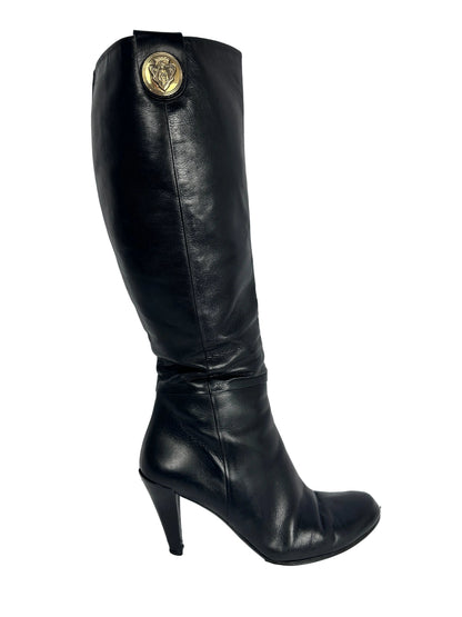 Black knee-high boot with a gold button on a white background