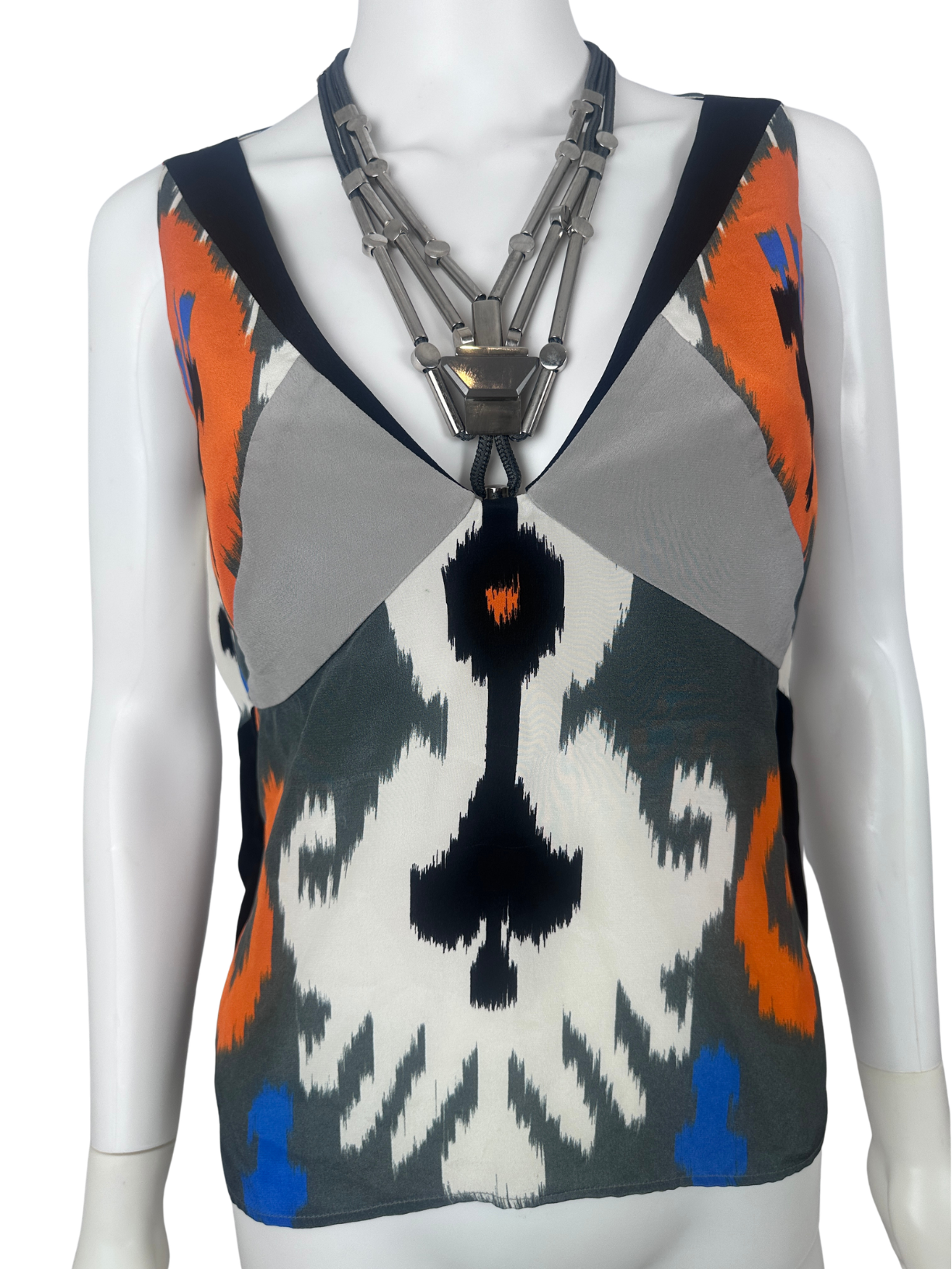 A sleeveless knit top with a geometric ikat pattern in gray, black, white, orange, and blue, displayed on a white mannequin torso with a chunky silver necklace.