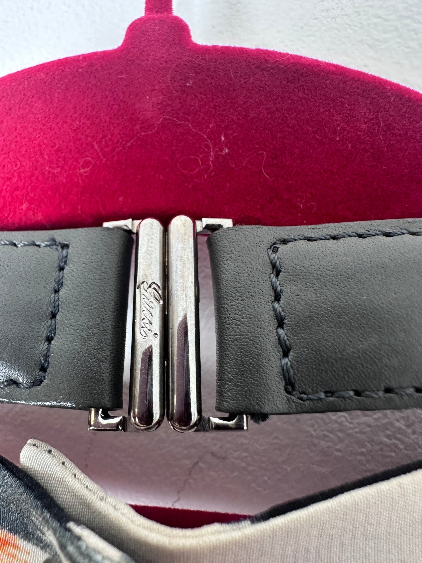 Close-up of a dark gray leather strap with a silver-tone metal buckle featuring the Guess logo, displayed on a red circular stand.