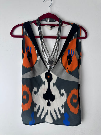 A patterned fabric pouch or bag with a geometric ikat design in gray, orange, white, black, and blue, featuring a silver metal zipper and a dark red strap, shown on a white background.