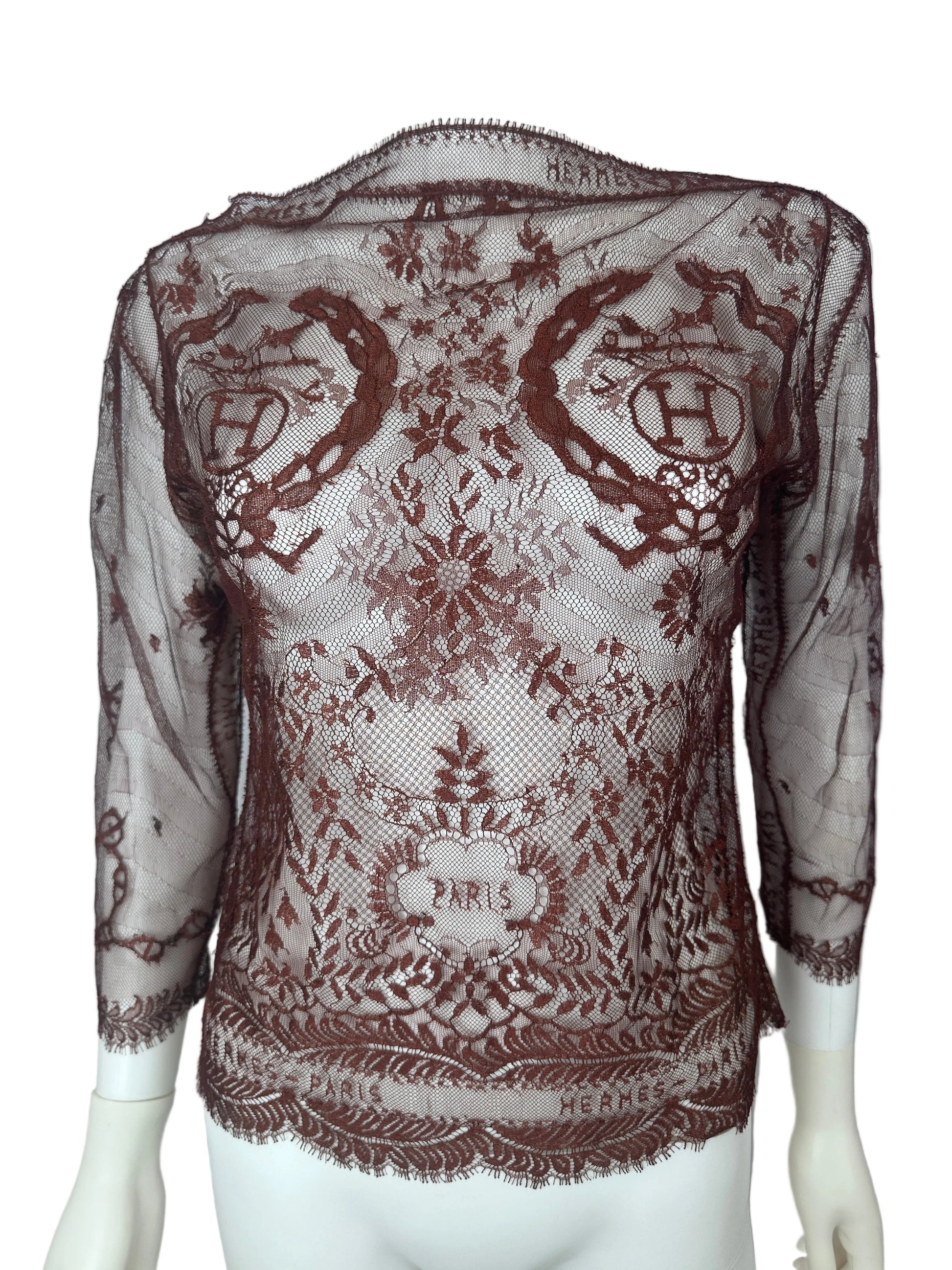 A sheer brown lace shawl with ornate floral and scroll patterns, draped over a white mannequin torso against a plain white background.