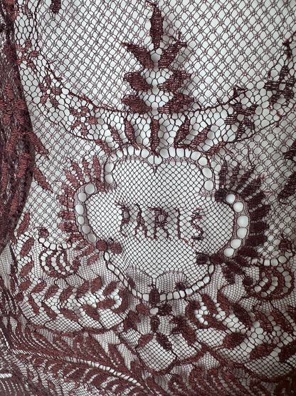 Close-up of a dark burgundy lace fabric with an intricate floral and sunburst pattern over a white mesh backing.