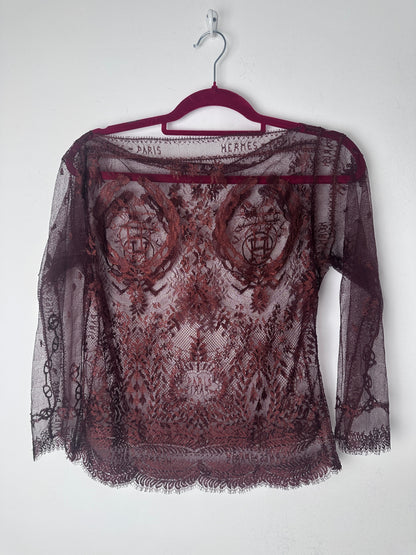 A sheer burgundy lace shawl with a floral pattern and fringed edges, draped over a matching burgundy hanger against a plain white background.