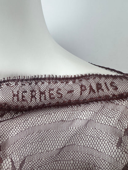 Close-up of a dark brown Hermès Paris lace trim draped over a white mannequin torso, showing the embroidered brand name and mesh pattern.