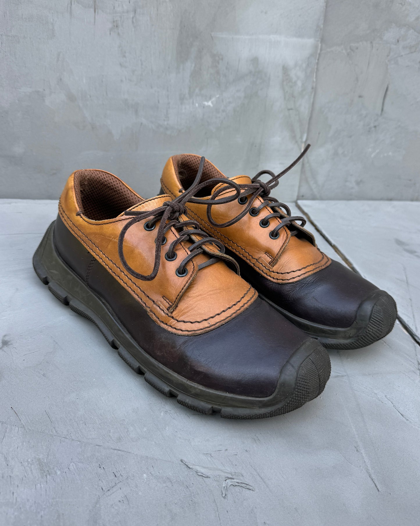Pair of brown and black shoes on a gray surface with a concrete wall background