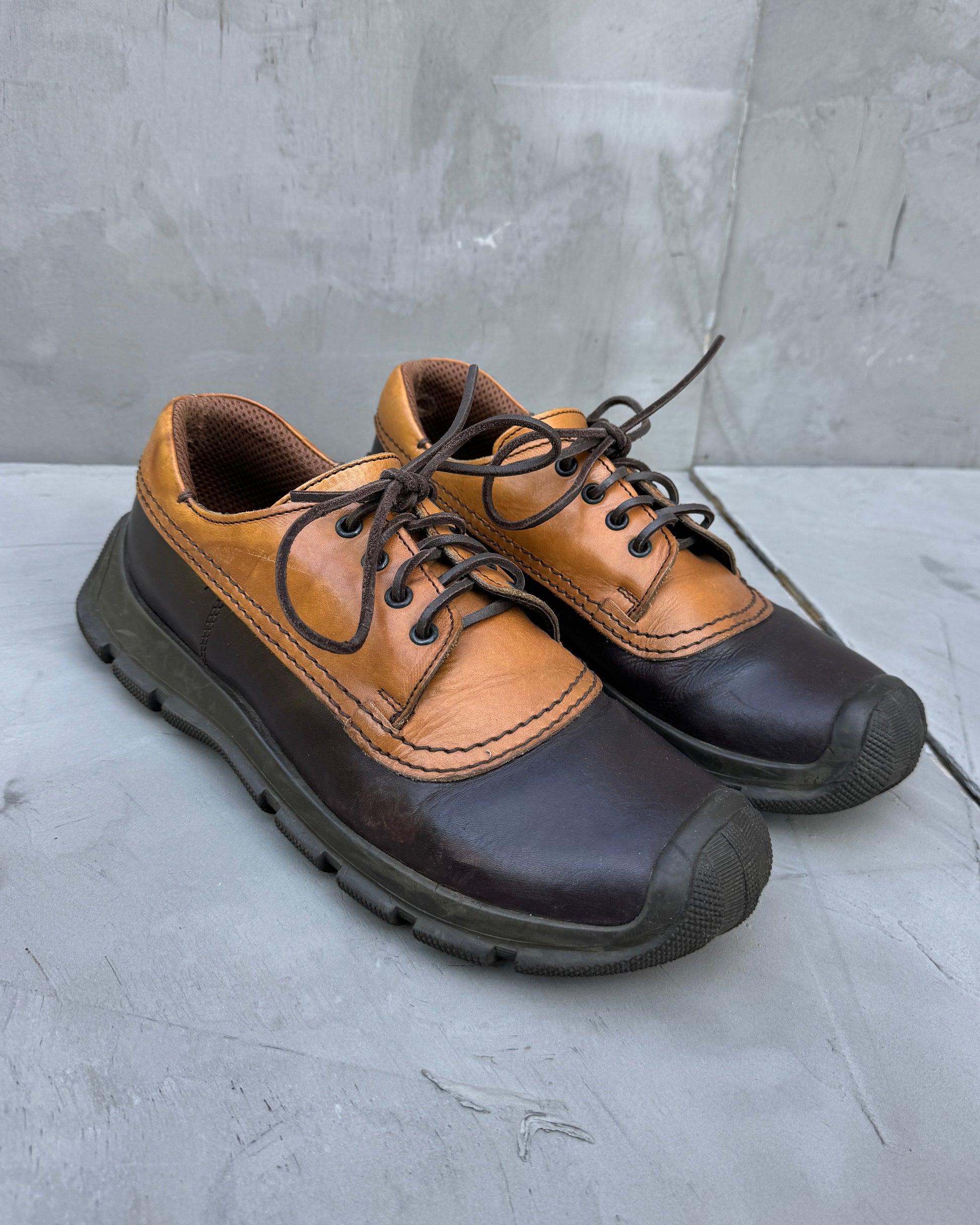 Pair of brown and black shoes on a gray surface with a concrete wall background
