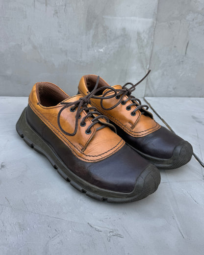 Pair of brown and black shoes on a gray surface with a concrete wall background