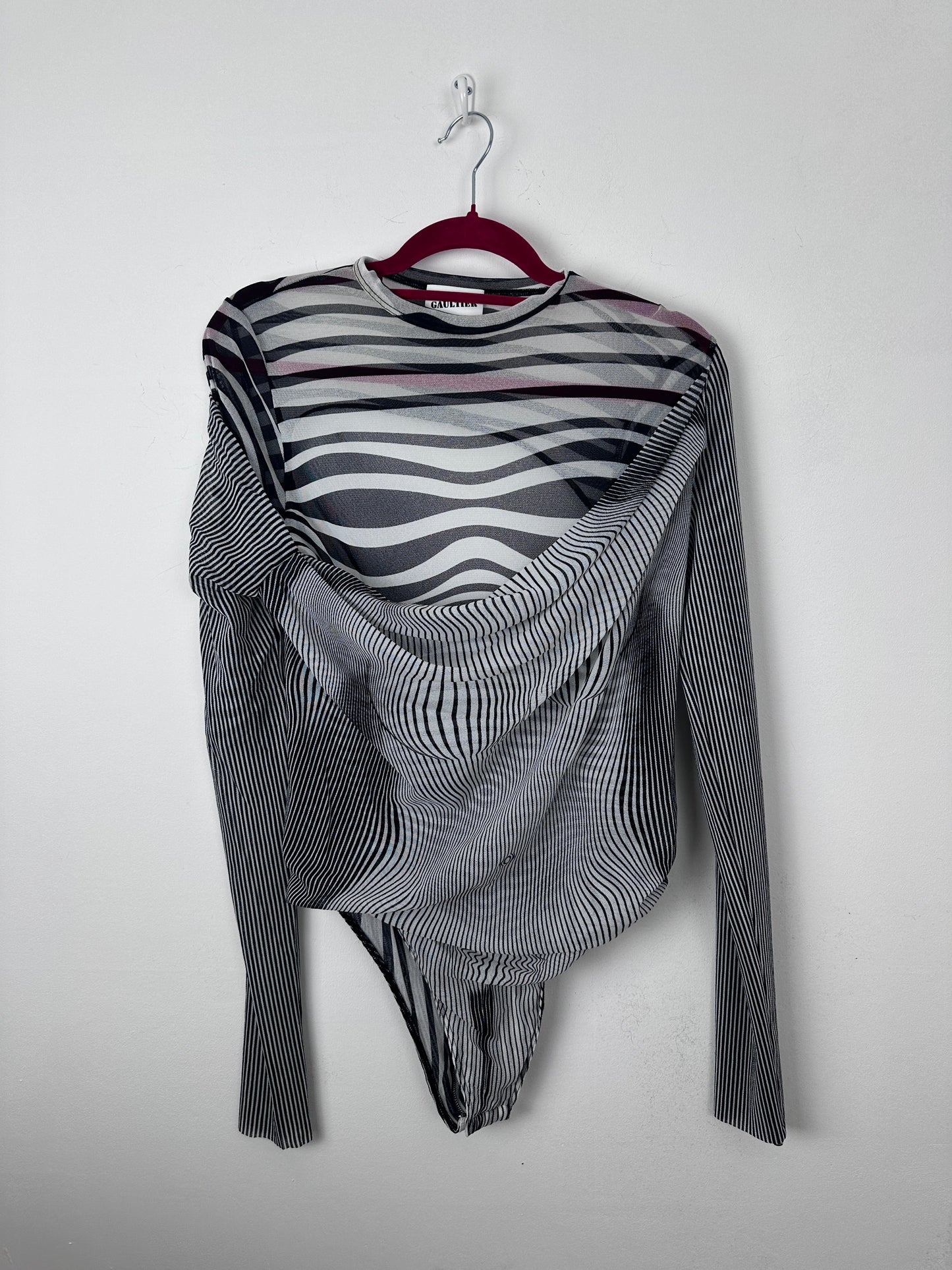 A long-sleeve striped knit top with black, white, and gray wavy patterns, draped on a red hanger against a plain light gray background.