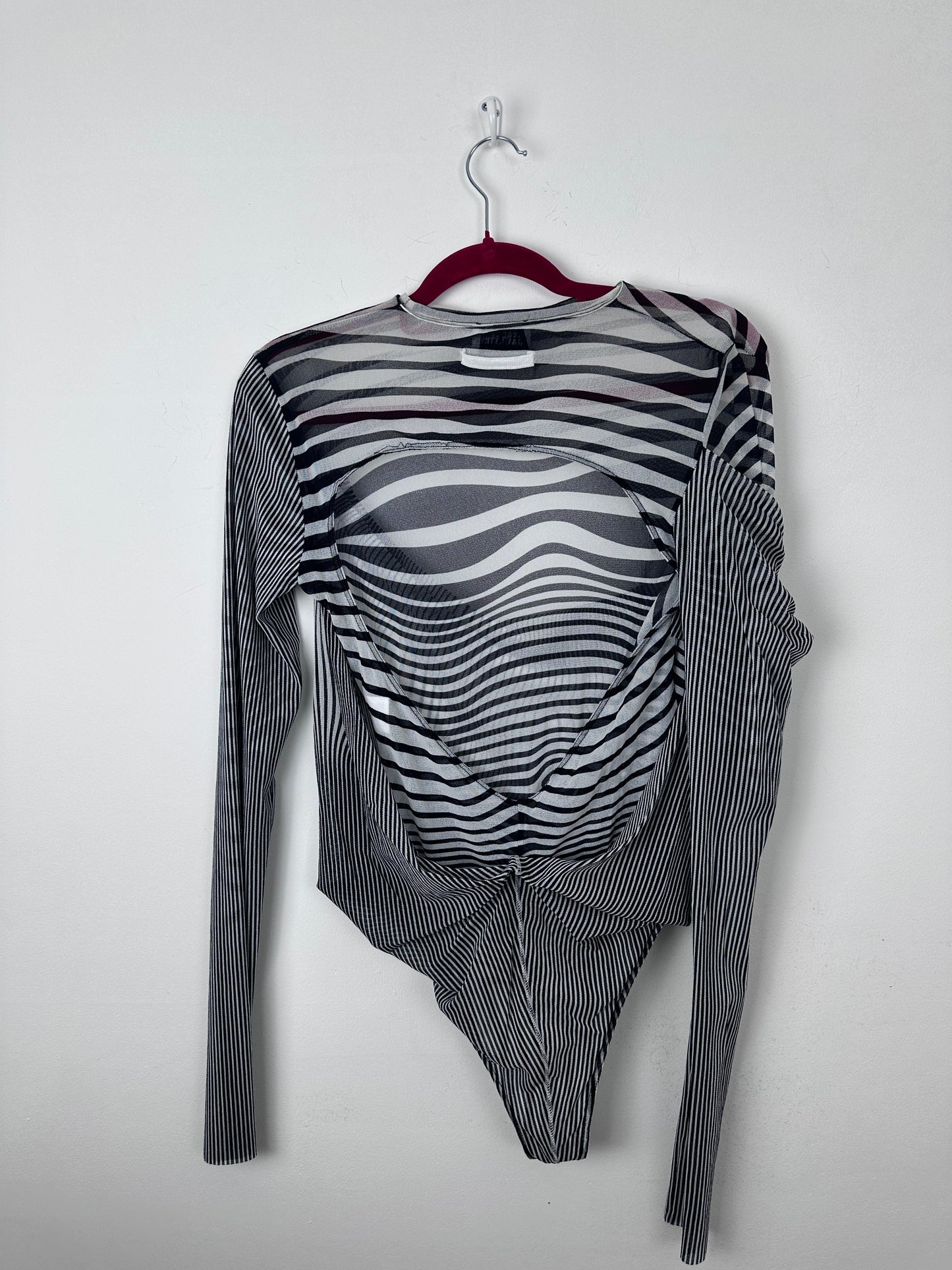 A long-sleeve sheer mesh top with a black and white wavy stripe pattern, laid flat on a white background with a red hanger.