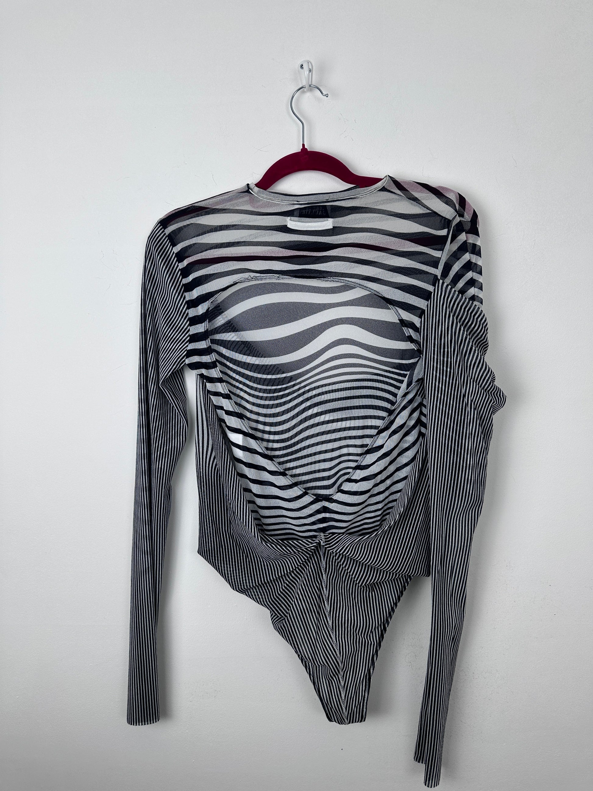 A long-sleeve sheer mesh top with a black and white wavy stripe pattern, laid flat on a white background with a red hanger.