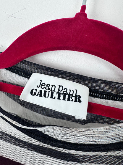 Close-up of a striped garment with a white fabric label reading 'Jean Paul Gaultier' in black text, showing red, white, black, and gray stripes.