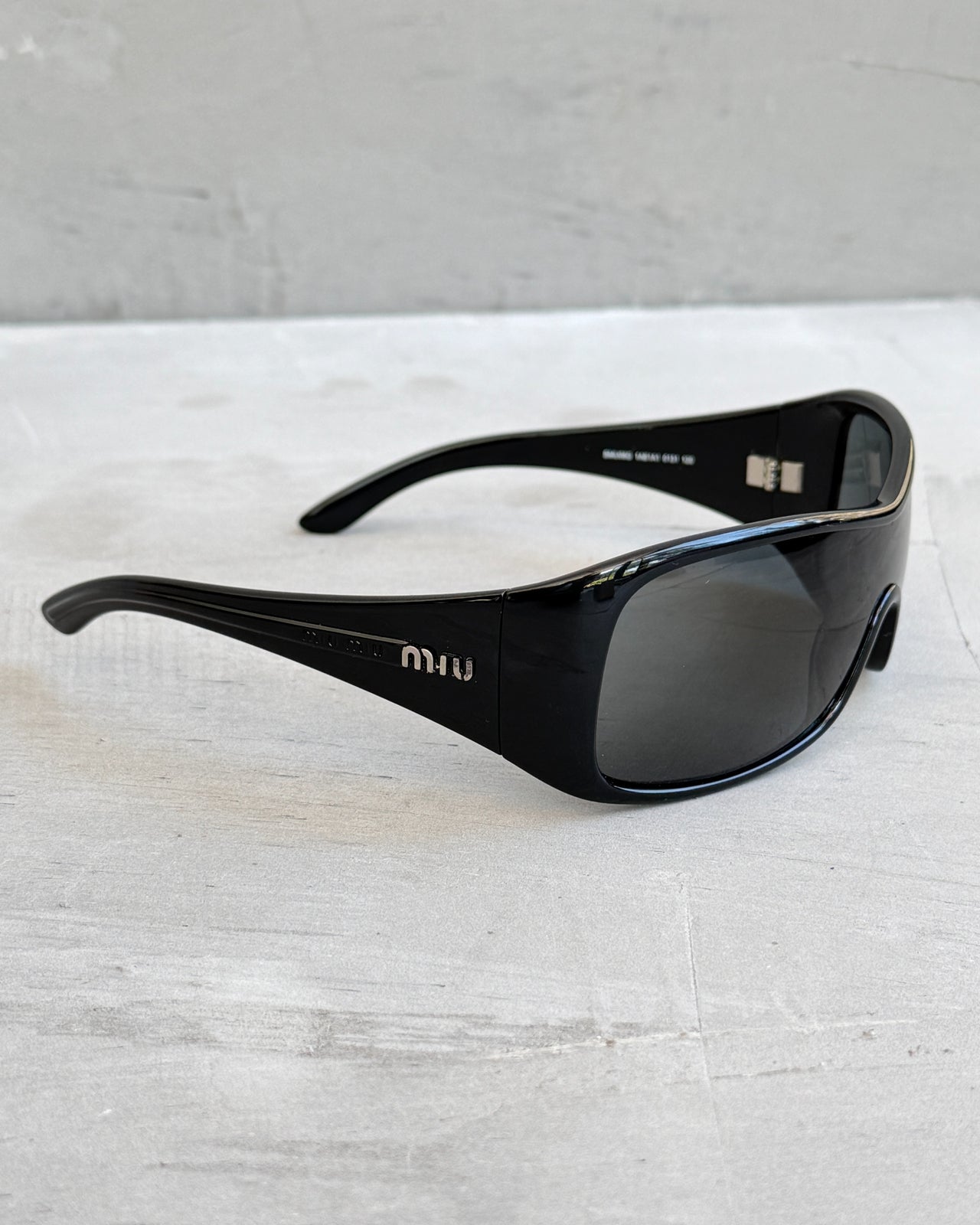 Miu Miu Black Wraparound Sunglasses-on a concrete background