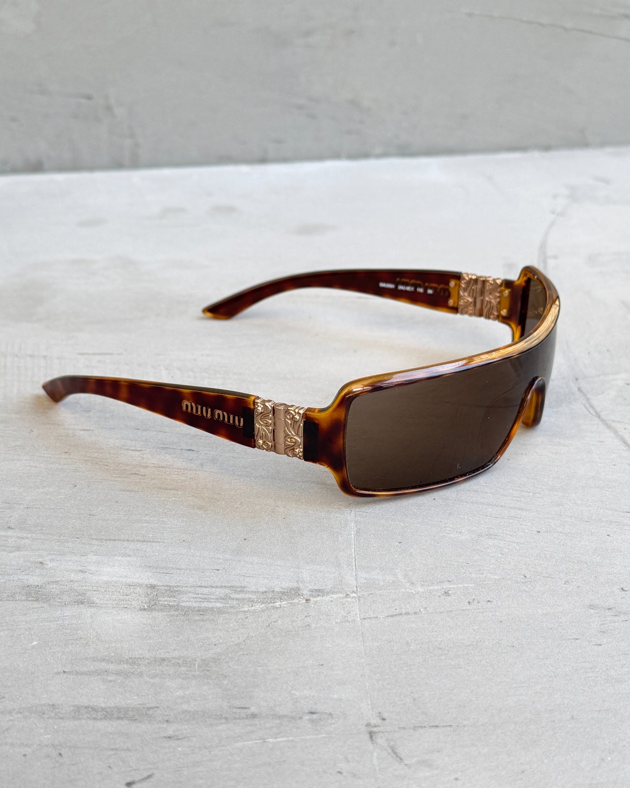 Miu Miu Brown Tortoiseshell Wraparound Sunglasses-on a concrete background