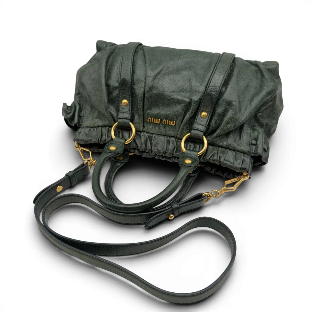 https://cdn.shopify.com/s/files/1/0564/9376/8855/files/Miu_Miu_Handtasche_Vitello_Lux_mit_Umhangegurt_aus_Leder_dunkelgrun_vintage7453.webp?v=1779291831
