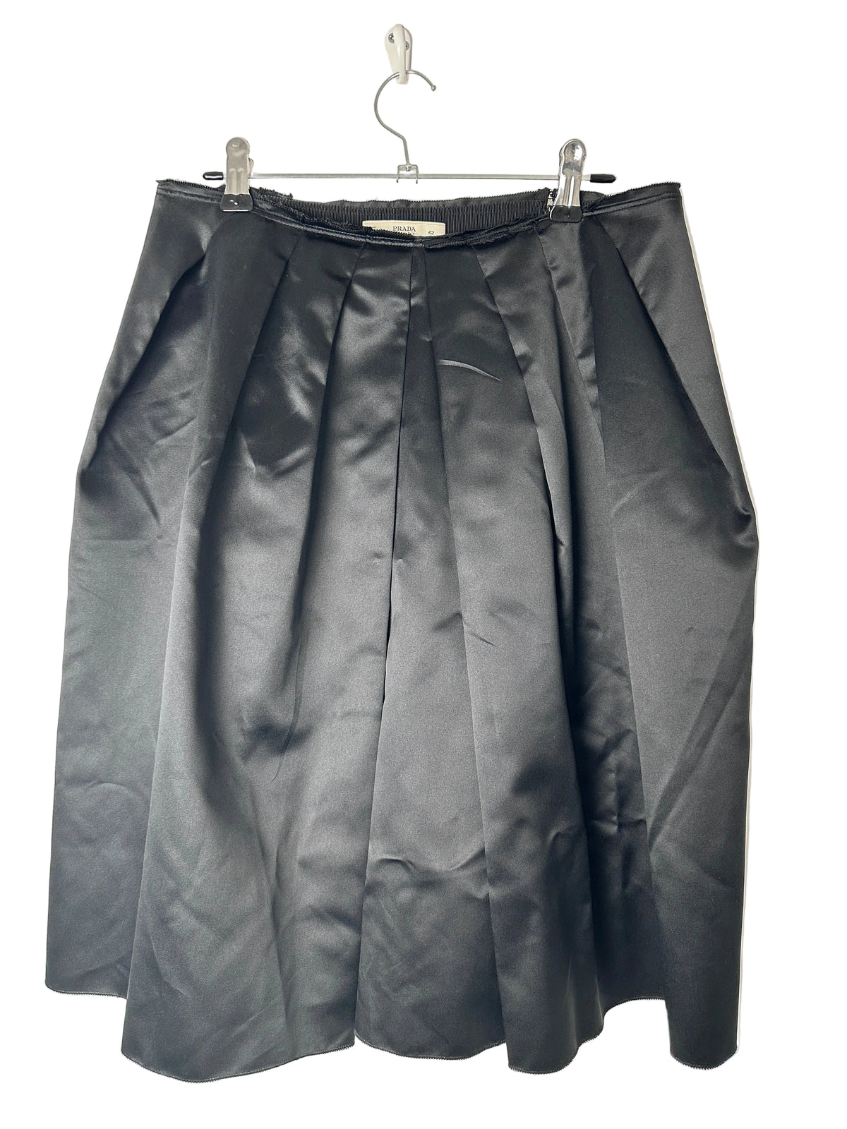 Folded black skirt on a clear hanger against a beige background