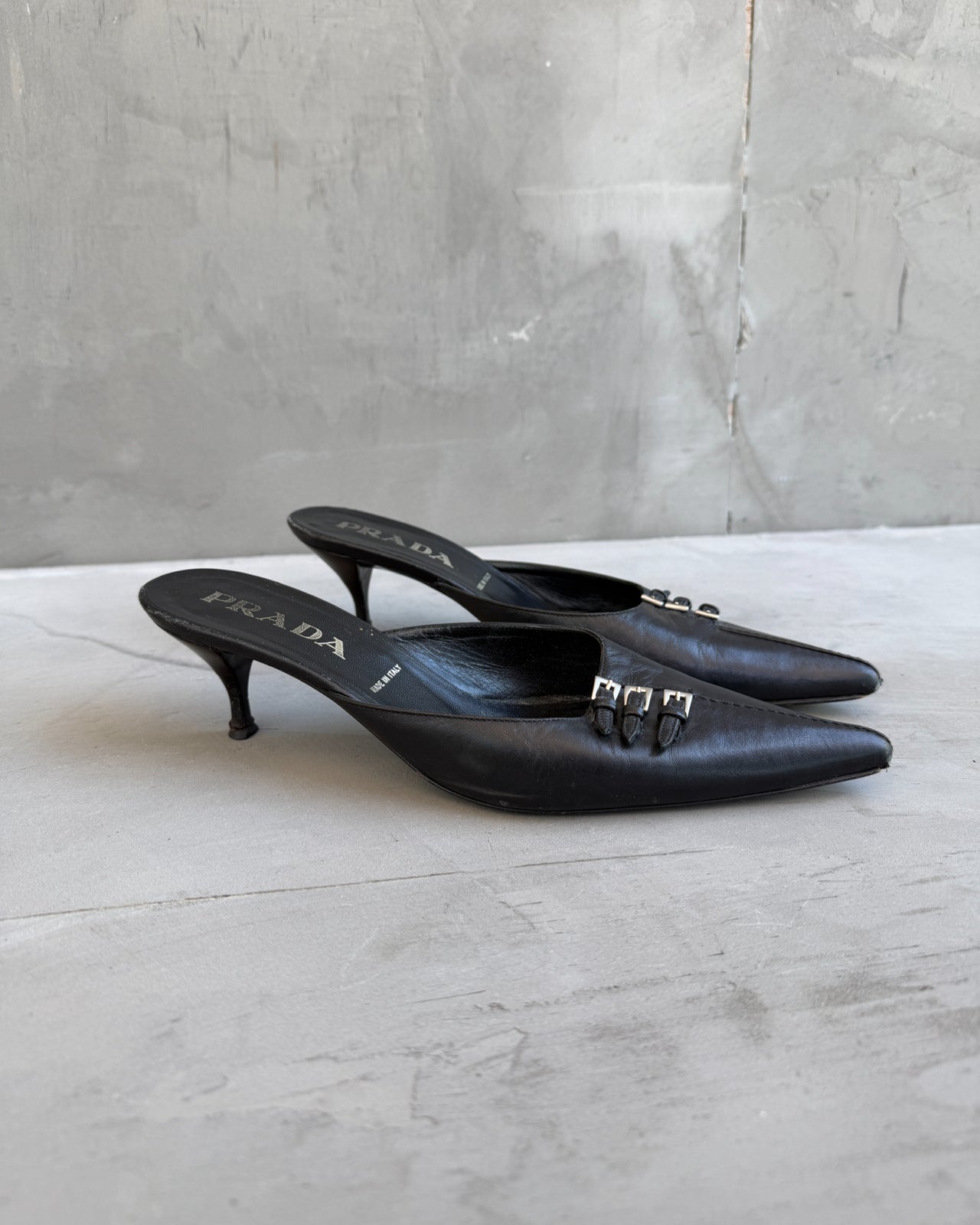 Prada Black Leather Triple Buckle Kitten Heel Mule – EU 37-on a concrete background