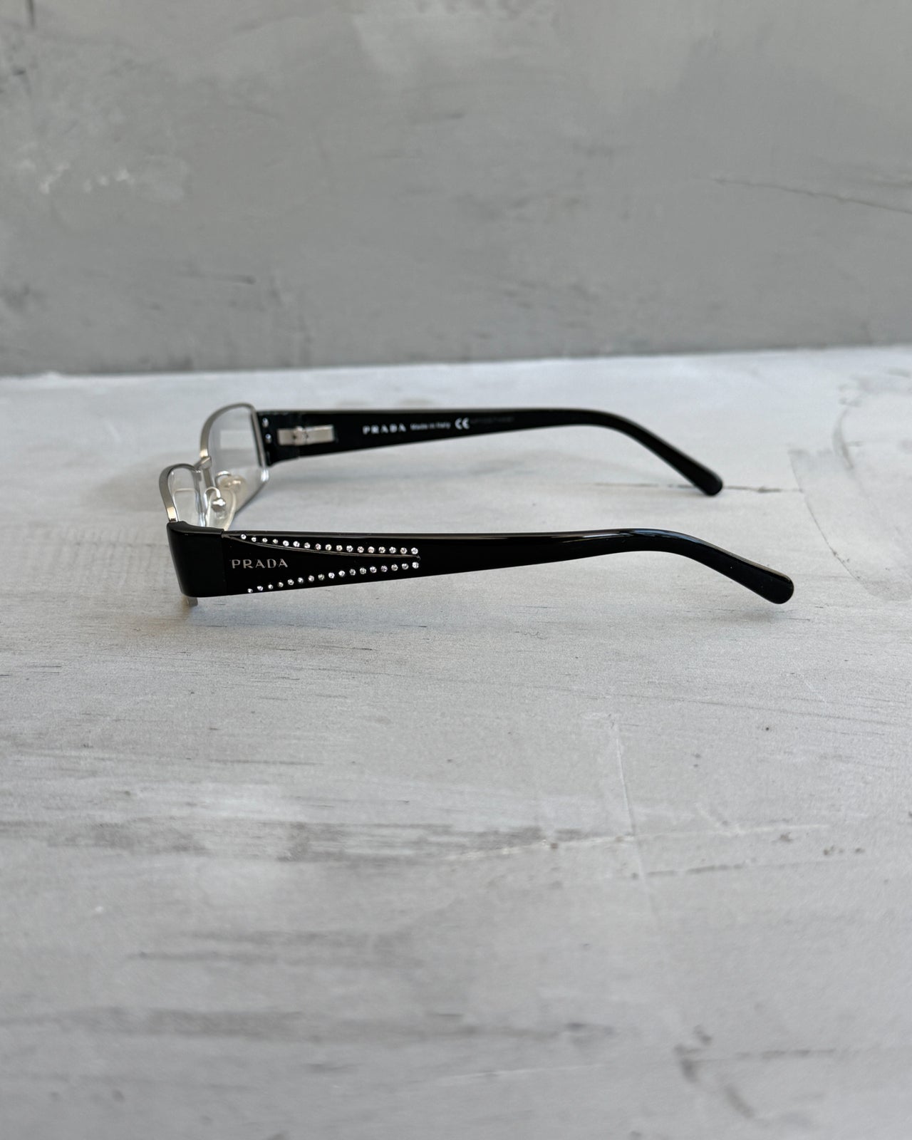 Prada Clear Lens Silver Frame Glasses-on a concrete background