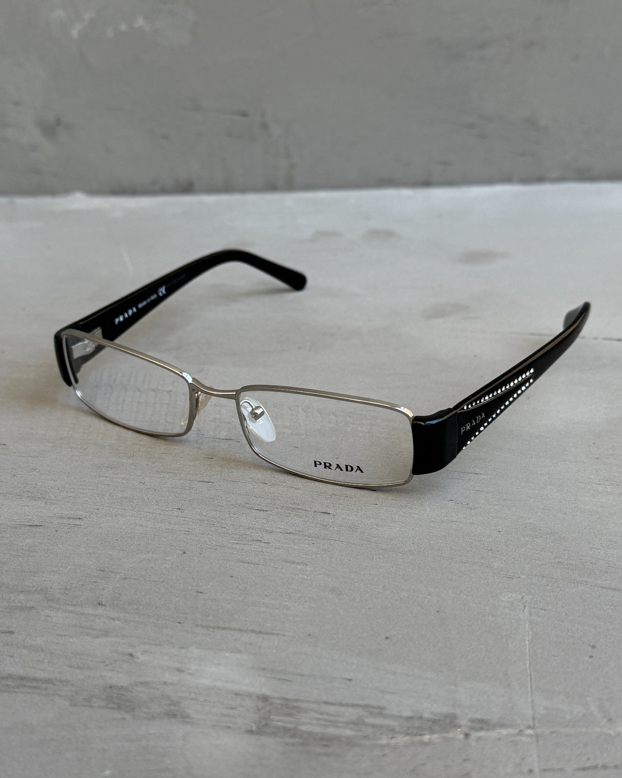 Prada Clear Lens Silver Frame Glasses-on a concrete background