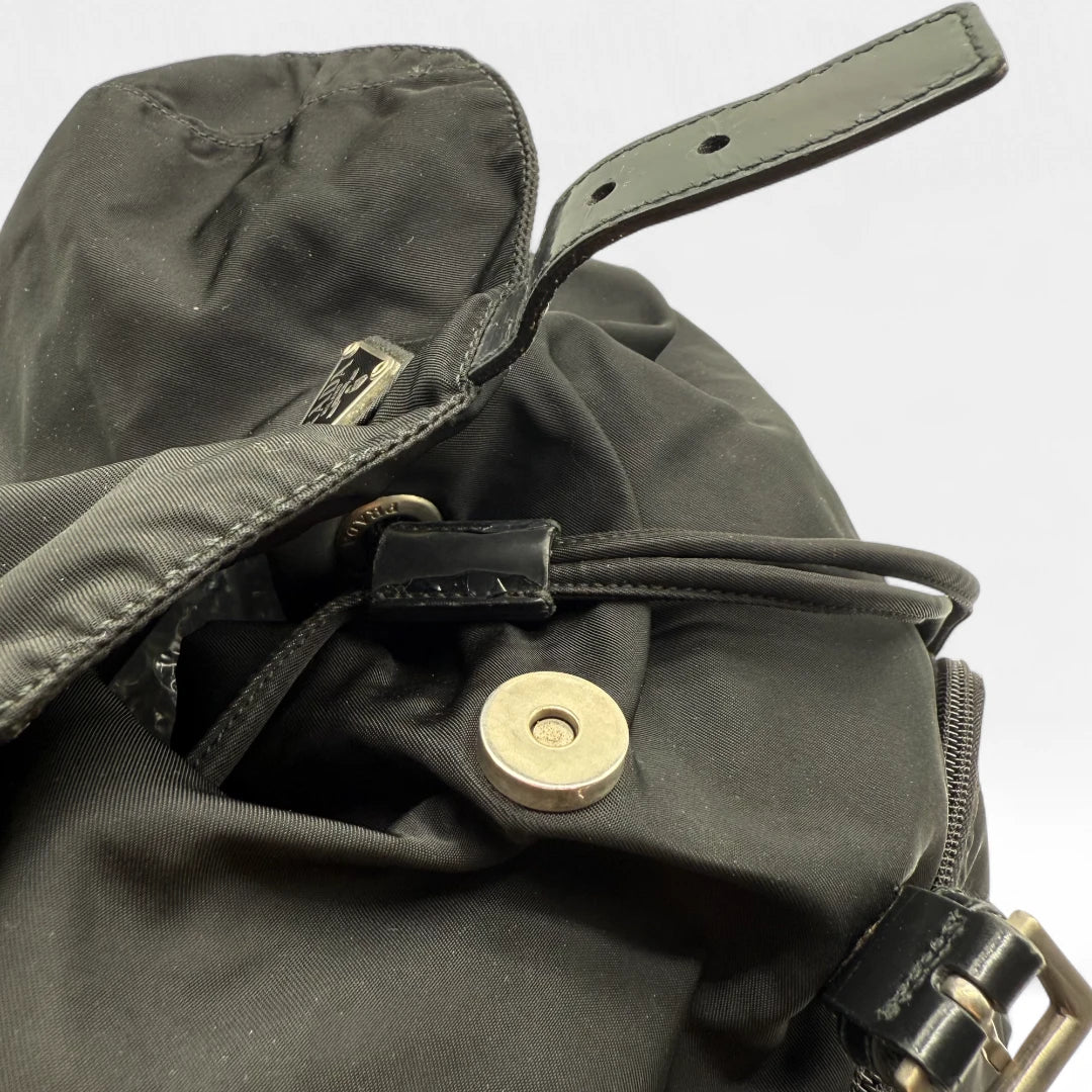 https://cdn.shopify.com/s/files/1/0564/9376/8855/files/Prada_Rucksack_mit_Schnalle_aus_Nylon_schwarz_second_hand_designer_backpack3171.webp?v=1753348226