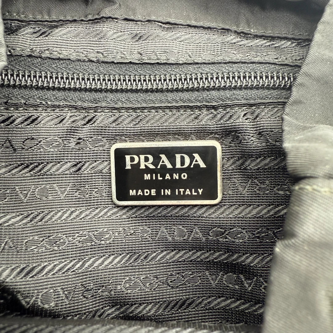 https://cdn.shopify.com/s/files/1/0564/9376/8855/files/Prada_Rucksack_mit_Schnalle_aus_Nylon_schwarz_second_hand_designer_backpack3174.webp?v=1753348227