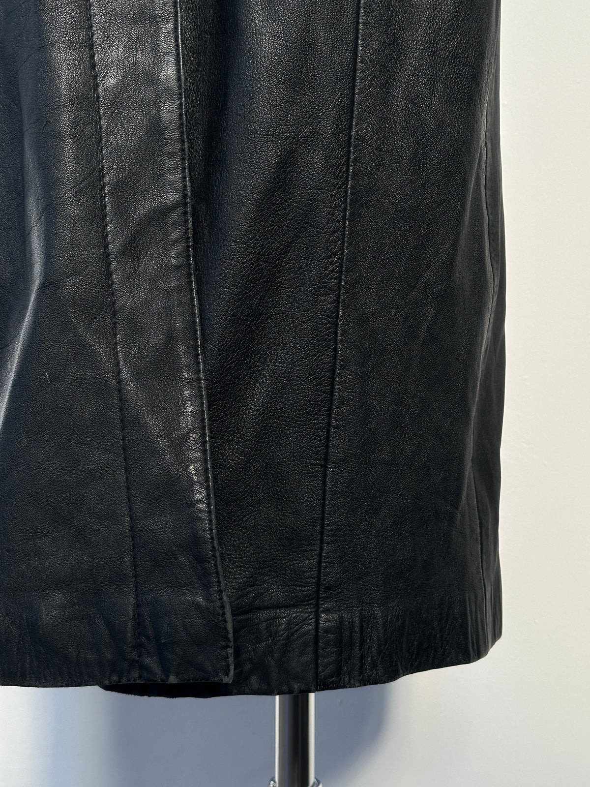 Vintage 1990s floor length leather trench coat, small size, with classic design and detailed collar, displayed hanging on a plain background.