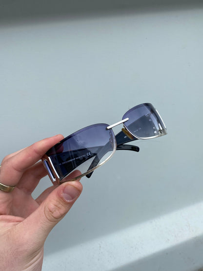 Dolce & Gabbana shield sunglasses with dark tinted lenses and sleek black frame on a white background.