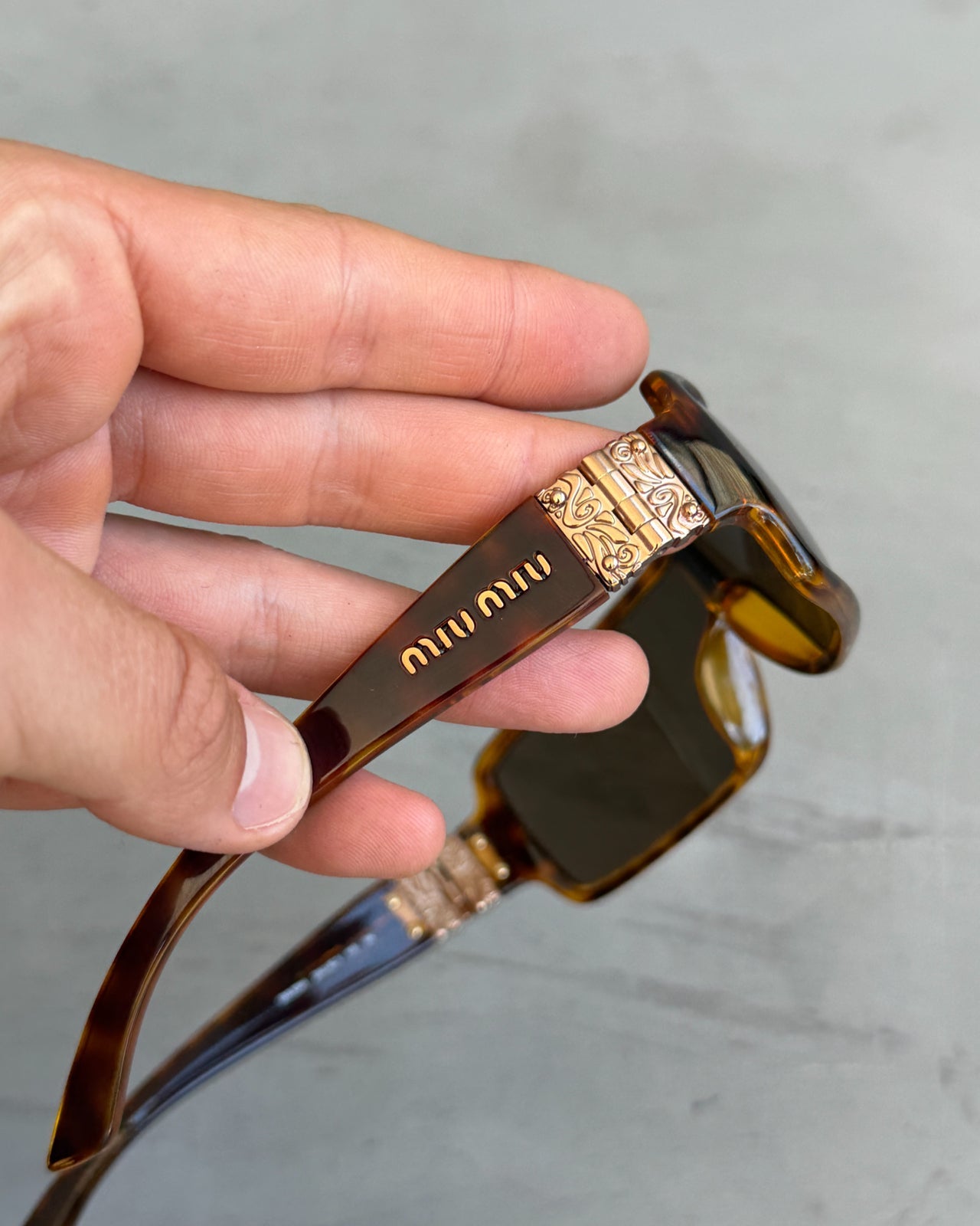Miu Miu Brown Tortoiseshell Wraparound Sunglasses-on a concrete background
